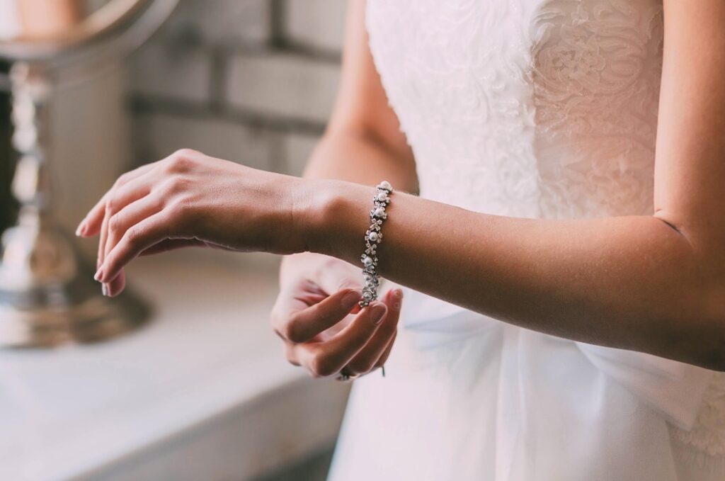 Braut legt sich ein Armband an – Detailaufnahme mit weichem Fokus auf die Hand. Nachhaltiger Hochzeitsschmuck im Einsatz für einen stilvollen und bewussten Hochzeitslook.